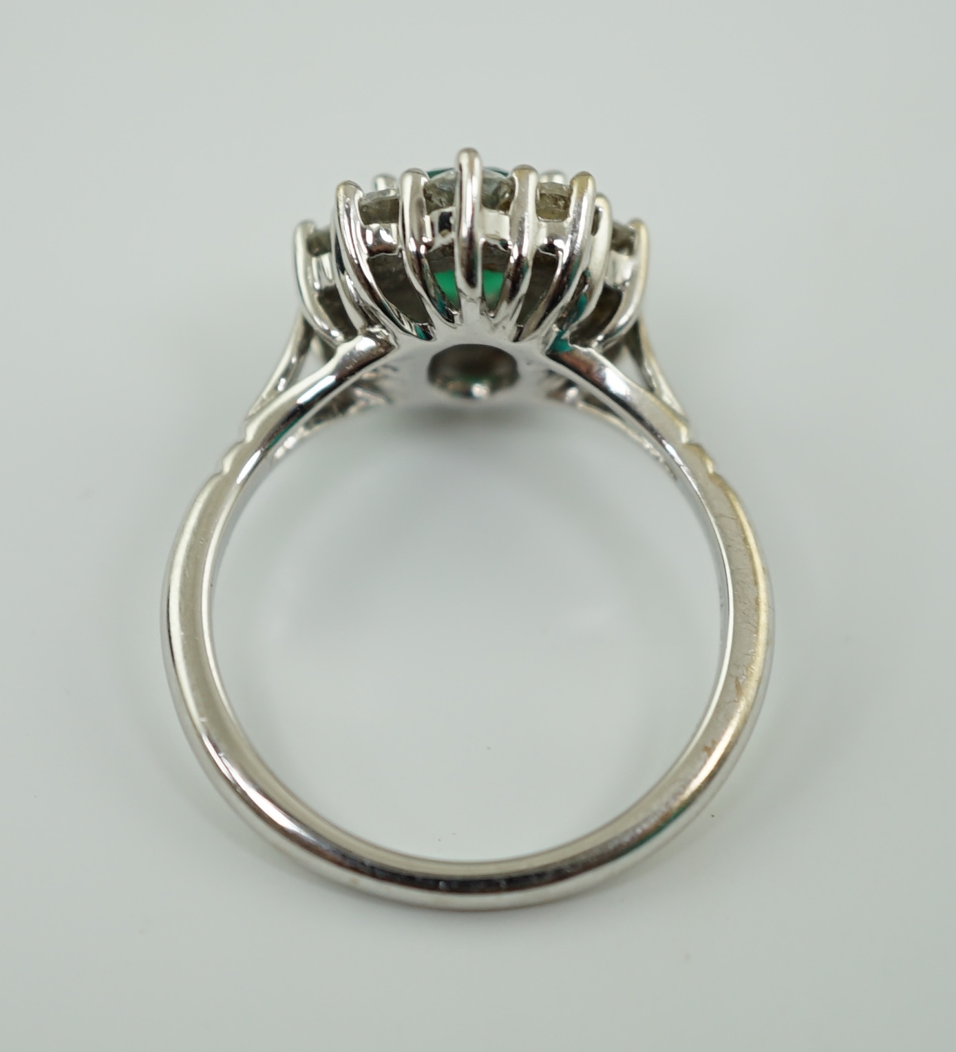 A modern 18ct white gold, single stone oval cut emerald and ten stone diamond set oval cluster ring